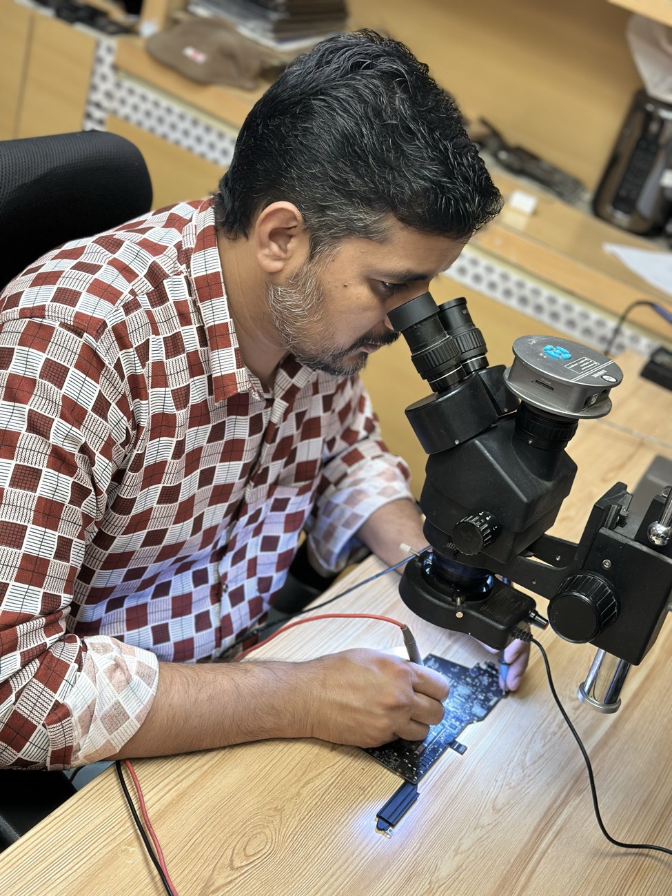 A Mak Doctor technician working on a MacBook logic board under a microscope